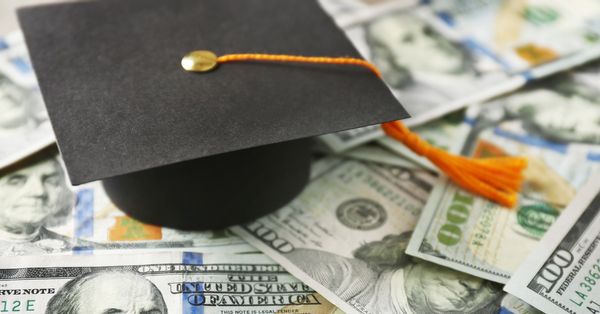 Graduation mortarboard hat on a pile of $100 bills