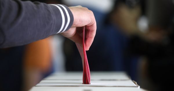 Older man voting at elections, hand putting ballot paper in ballot box.
