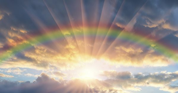 Rainbow in a cloudy sky with the sun shining through