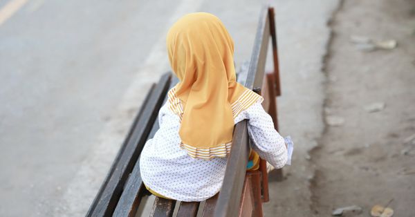 Young girl in hijab sitting on a bench