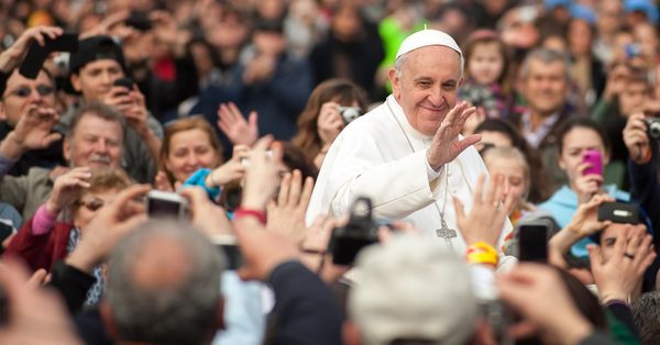 Smiling Pope Francis surrounded by a crowd.