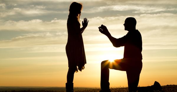 Silhouette of a man kneeling to propose to a woman.