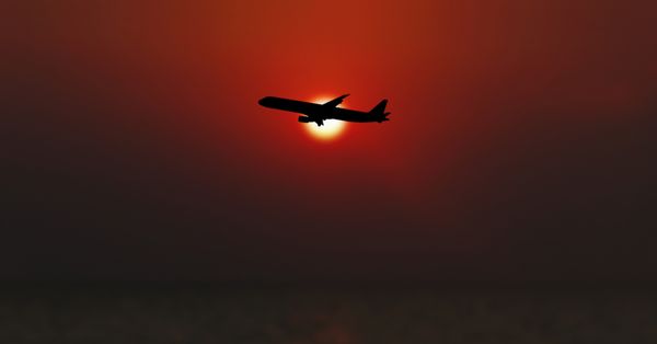 Airplane flying with sun in background.