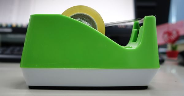 A bright green Scotch tape dispenser on an office desk.