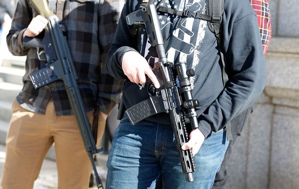 Two men with their firearms listen to speakers at a protest to new gun legislation