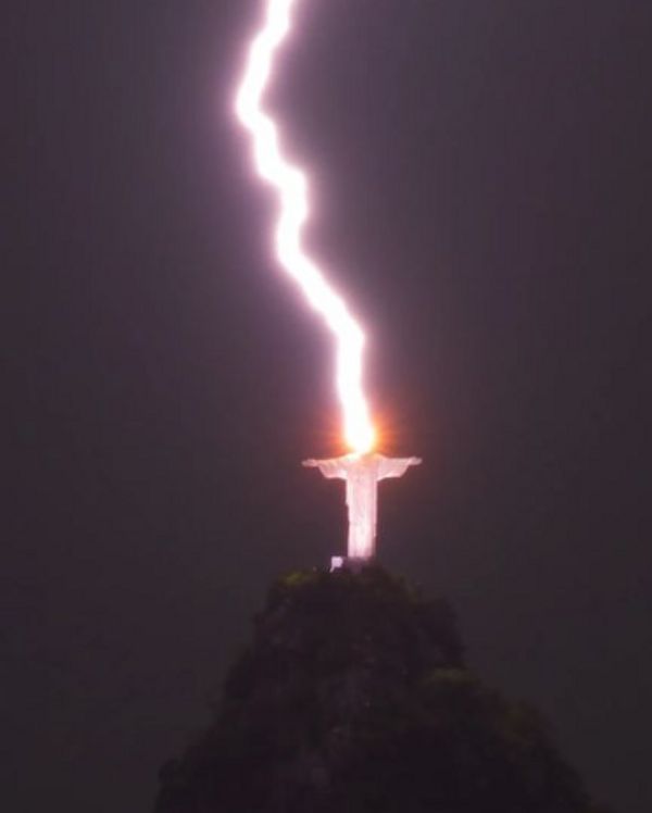 A thick bolt of lightning hits a large statue that's located on a cliff.