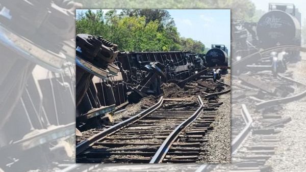 A photo shows a train on its side off the tracks near trees.