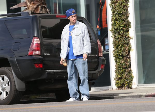 A white man holding a coffee cup looks to cross a street.