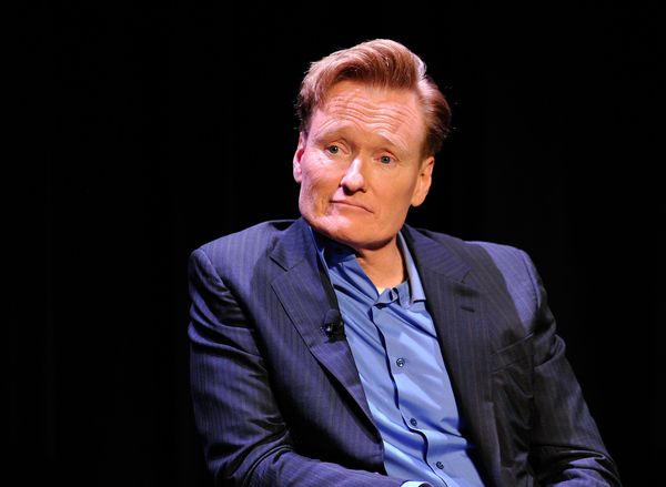 A white man in a blue suit sits and looks towards the left.