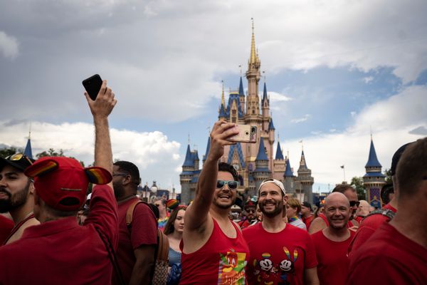 Two men wearing red shirts pose for a selfie surrounded by a crowd of people. Cinderella's Castle can be seen in the background.