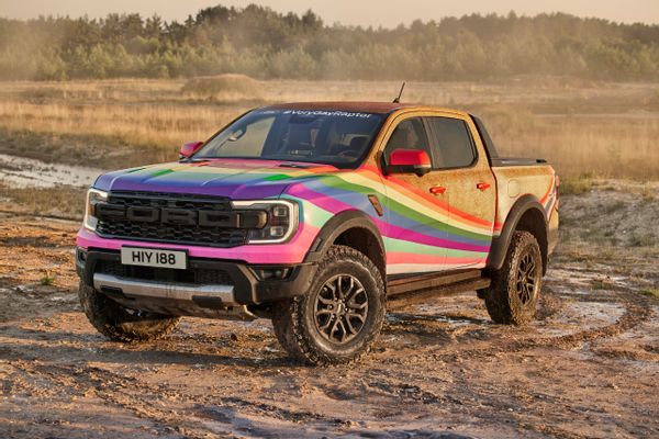 A gold truck with rainbow colors is parked on a dirt road.