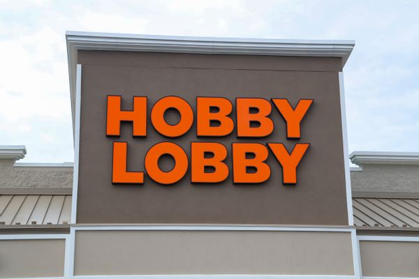 A brown building with the words "Hobby Lobby" in orange is pictured. In the background is a light blue sky with white clouds.