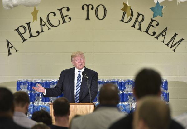 A white man stands at a podium in front of a crowd. He stands under words that say, "A Place To Dream." 