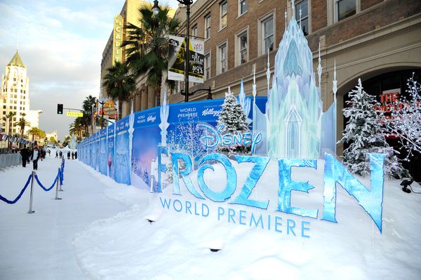 Outside sits a sign that says "Disney Frozen World Premiere" in icy blue. It rests on a bank of fake snow. Fake snow also sits on the sidewalk near it, where you can see people walking.