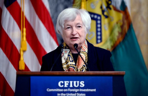 A white woman with white hair stands before a podium that says Committee on Foreign Investment in the United States (CFIUS).
