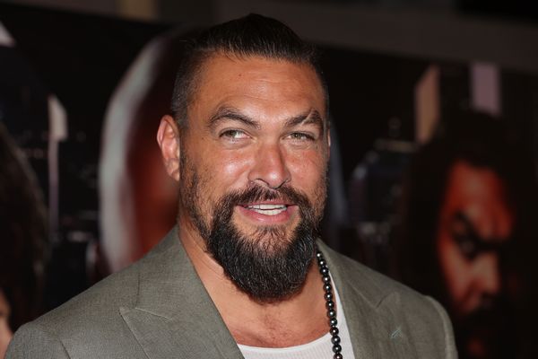 A Polynesian man with a beard wearing a gray suit is photographed smiling.