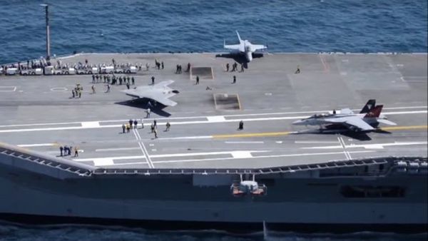 Three planes are on a large ship. People are also on the ship, with many gathered towards the left side of the boat.