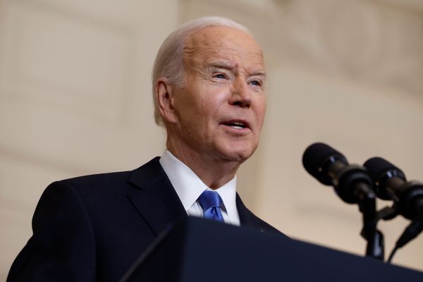 A white man wearing a dark blue suit speaks before a podium.