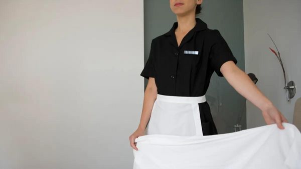 A person wearing a black and white uniform holds a sheet in a room.