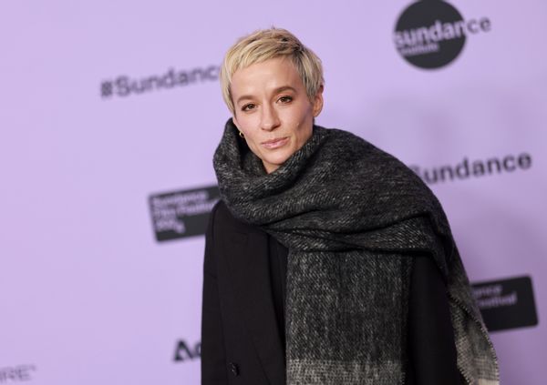 A white woman wears a large gray scarf with a black jacket as she looks at the camera.