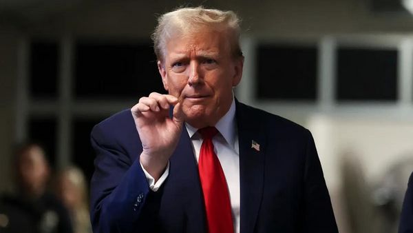 A white man wearing a blue suit holds the index and thumb of his left hand close together.