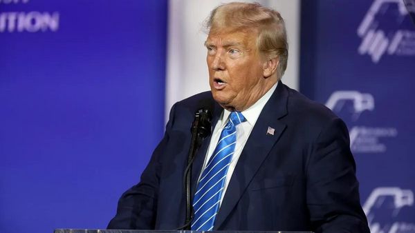 A white man wearing a dark blue suit speaks at a podium.