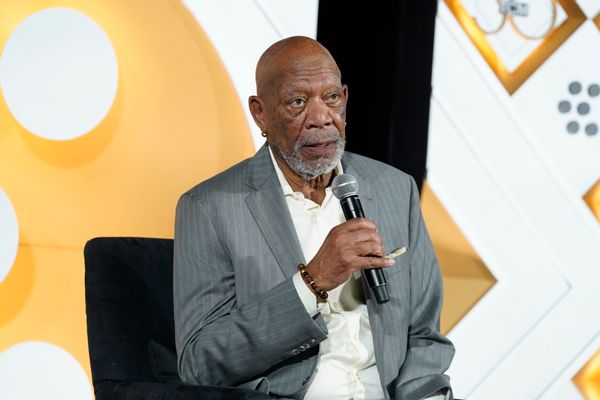 A Black man wearing a gray suit holds a microphone.
