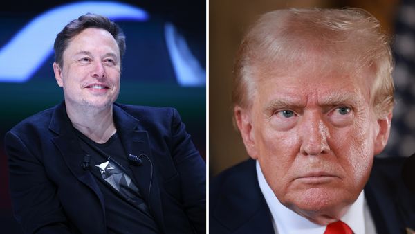 A white man wearing a blue suit smiles next to another white man wearing a black suit.