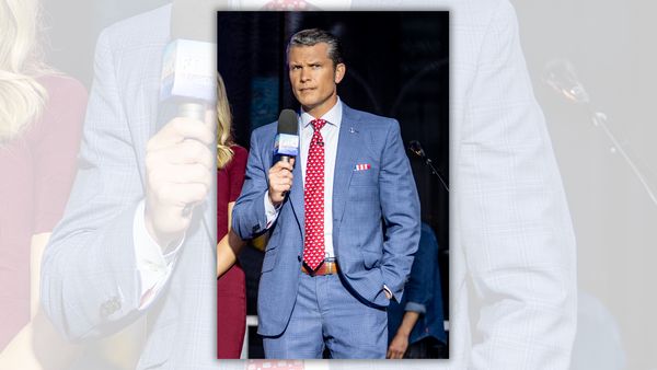 A white man wearing a blue suit holds a microphone in his left hand.