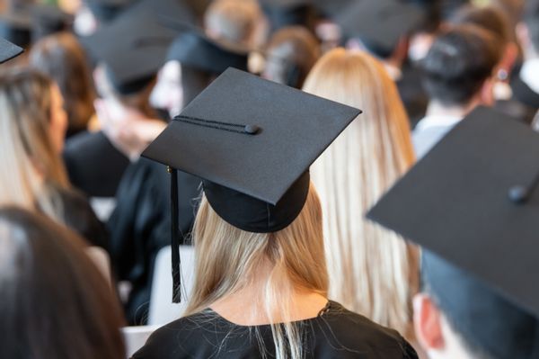 A picture of the backs of people wearing black graduation caps and gowns. 
