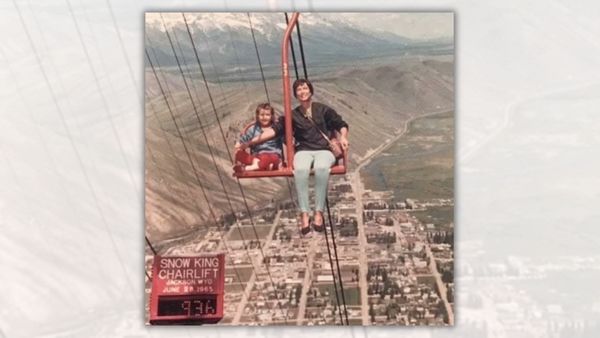 A photo shows an adult holding one arm in front of a child in a chairlift. Slightly below the two people was a sign that identified the photo as being taken at the Snow King Chairlift in Jackson, Wyoming, on June 29, 1965. 
