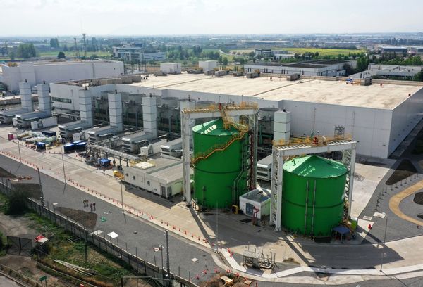 Two large cylindrical green tanks next to a white warehouse building. 