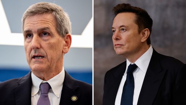 Two white men wearing black suits are pictured next to each other. One is looking forward + speaking, while the other on the right is looking towards the left side.