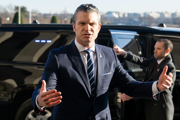 A white man wearing a blue suit spraks with his arms outstretched.
