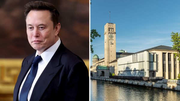 A white man wearing a blue suit is pictured next to a large building pictured along a body of water.