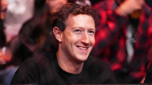A white man smiles while looking forward. People can be faintly seen sitting behind him.