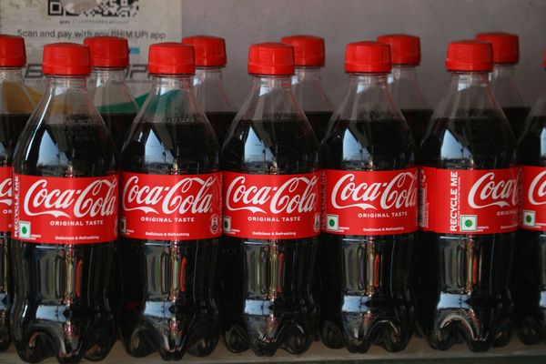 Bottles of Coca-Cola, with red caps and red Coca-Cola labels with white lettering, in a row. 