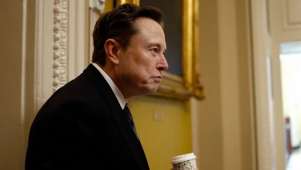 The side of a white man wearing a black suit holding a coffee cup is shown.