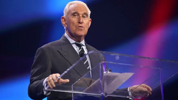 A white man wearing a gray sucker stands at a clear podium.