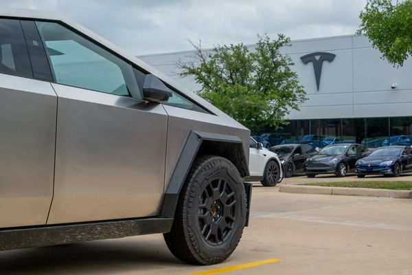 A silver angular truck known as a Cybertruck in front of an office building labeled "T" for Tesla. 