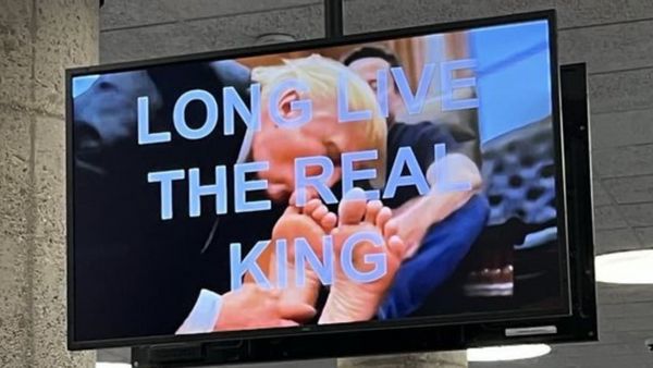 A TV shows a white man sucking on another white man's toes. White text on top of the image says, "LOVE LIVE THE REAL KING." 