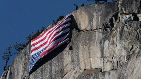 A red, white and blue flag is hung upside down on a large rock formation.