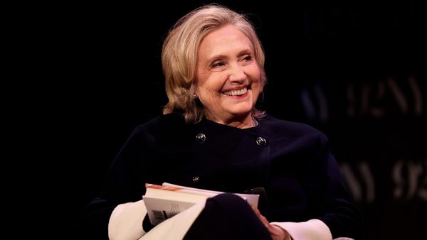 A white woman wearing a dark blue top sits and smiles while looking to the right.