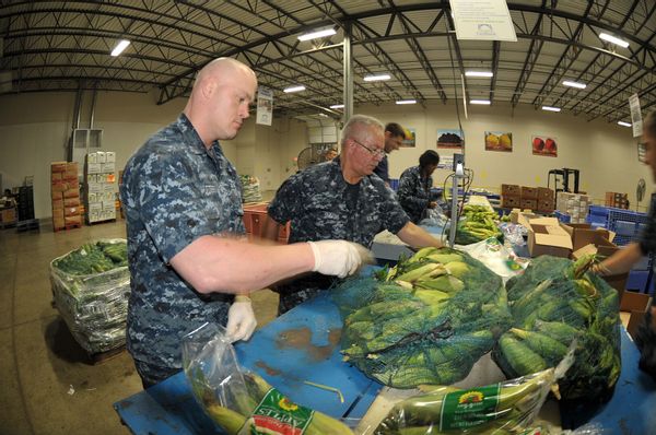 Two  people wearing military uniforms pack produce in a warehouse.