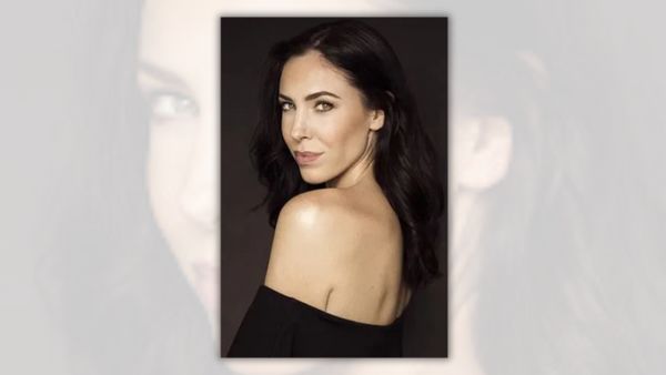 A white woman wearing a black top looks over her left shoulder towards the camera.
