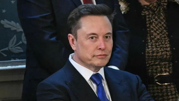 A white man wearing a blue suit looks towards the camera.