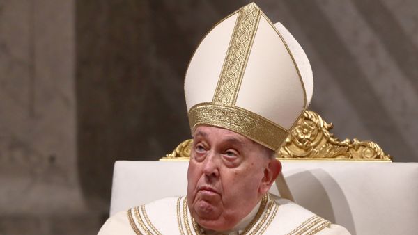 A white man wears a large white hat with gold accents while sitting down.
