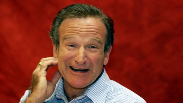 A white man smiles at the camera. His left hand wearing a wedding ring is touching his left cheak.
