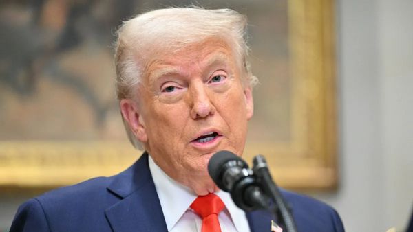 A white man wearing a blue suit speaks into a microphone.
