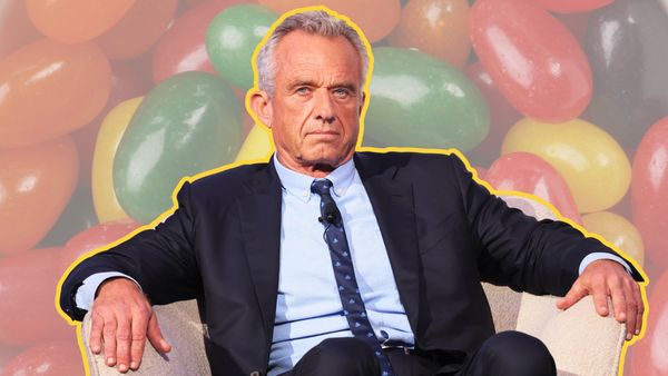 A white man wearing a blue suit sitting down in a white chair is shown in front of a background of jellybeans that are colored green, blue, orange, red and other colors.